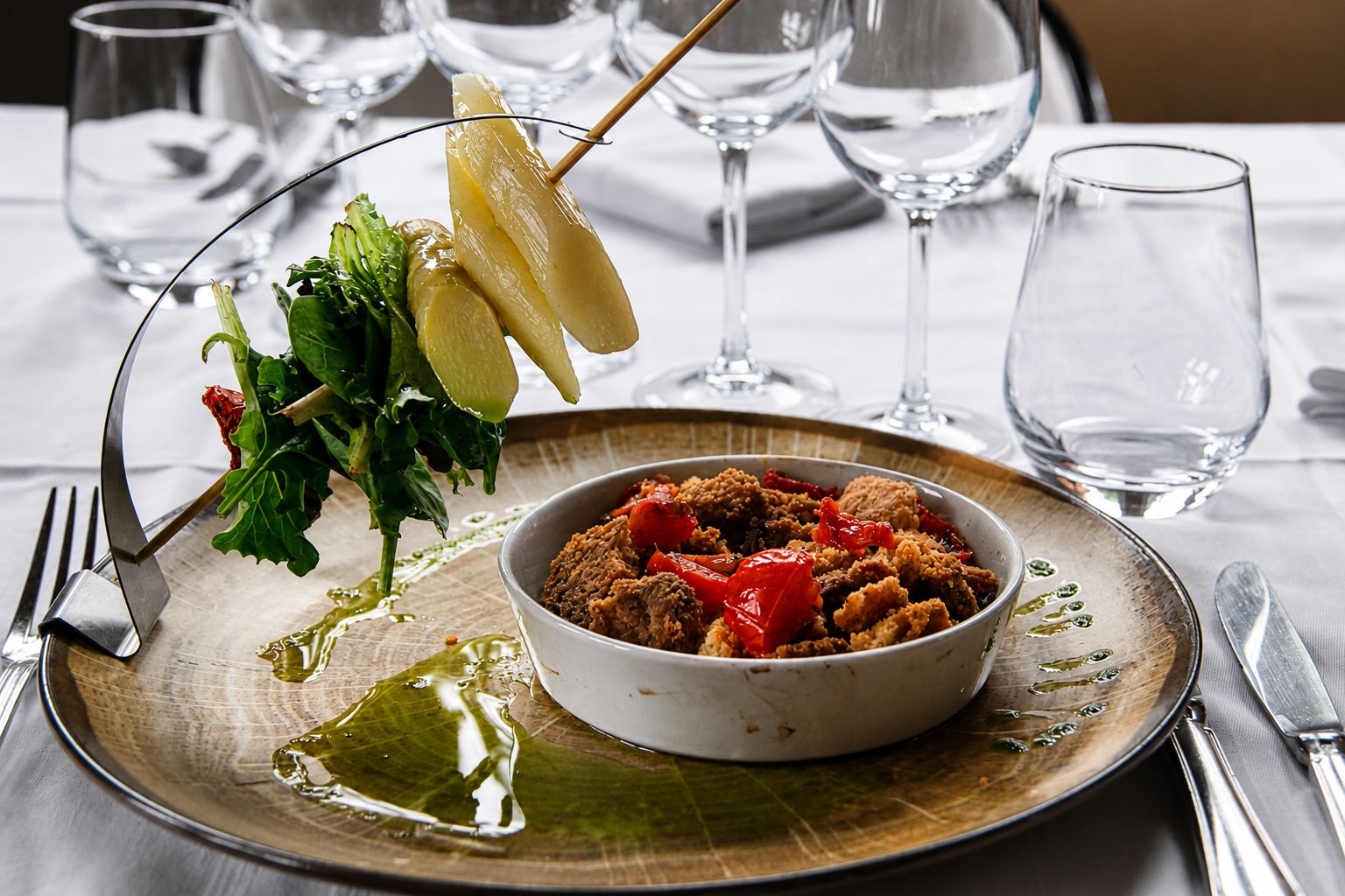 A meal with a bowl of meat and vegetables, a plate with a green sauce, and a fork on a table with glasses and cutlery.