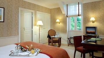 Habitación de hotel con cama, bandeja de desayuno, escritorio, computadora y ventana con vistas a follaje.