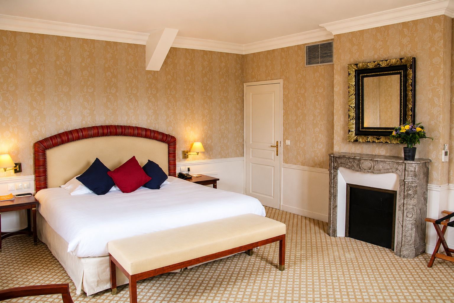 Una camera d'albergo con un letto grande, un camino, uno specchio e un tappeto a motivi.