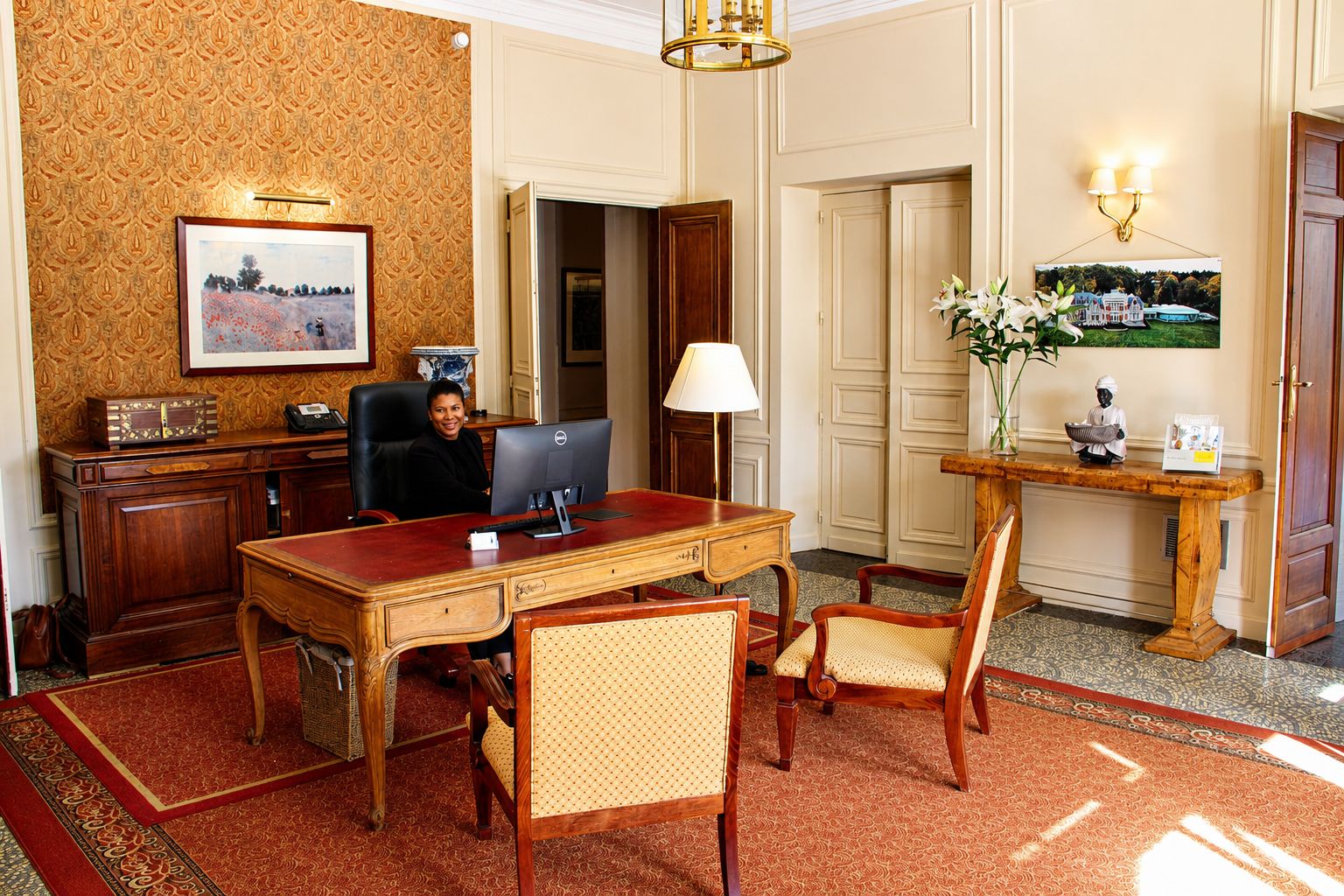 Un ambiente de oficina formal con escritorio, computadora, sillas, lámpara y un jarrón decorativo.