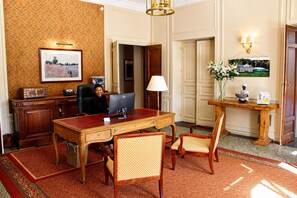 Un ambiente de oficina formal con escritorio, computadora, sillas, lámpara y un jarrón decorativo.