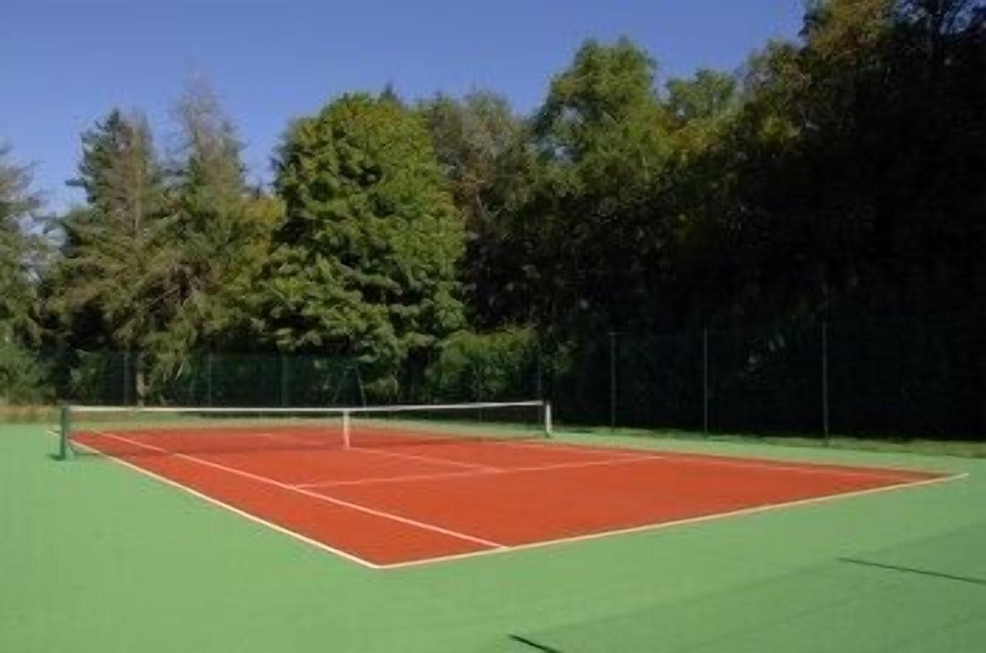 A tennis court with a net, surrounded by trees.