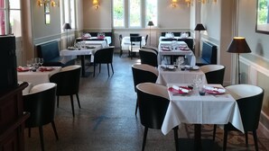 Un restaurante con varias mesas dispuestas para comer, que presenta una decoración clásica con vigas de madera en el techo y luz natural que entra por grandes ventanales.