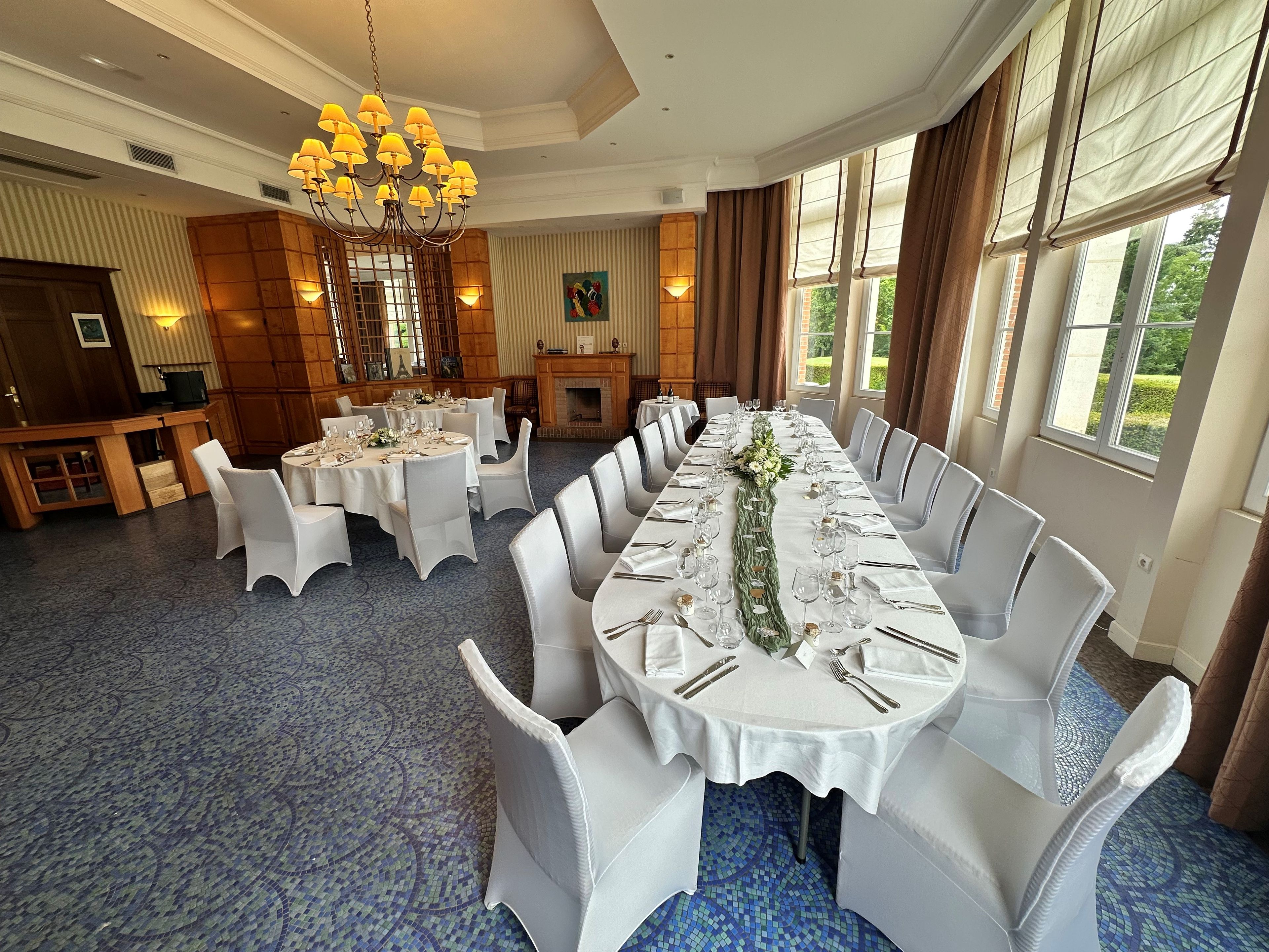 A banquet hall with round tables, white chairs, a chandelier, and a fireplace.