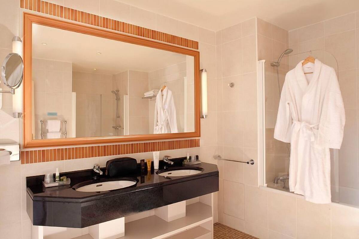 A modern bathroom with two sinks, a large mirror, and a walk-in shower.