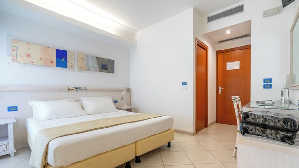 Una habitación de hotel con una cama, una mesita de noche y una maleta sobre un aparador.