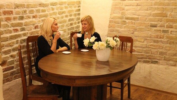 A round wooden table with two chairs, a vase with white flowers, and a brick wall in the background. - Alexa Old Town (Vilnius)