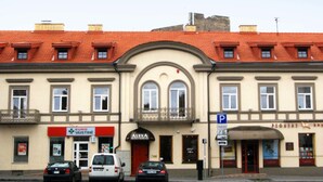 A building with a red-tiled roof, a central entrance with an arch, and a sign for a pharmacy and a hotel. - Alexa Old Town (Vilnius)