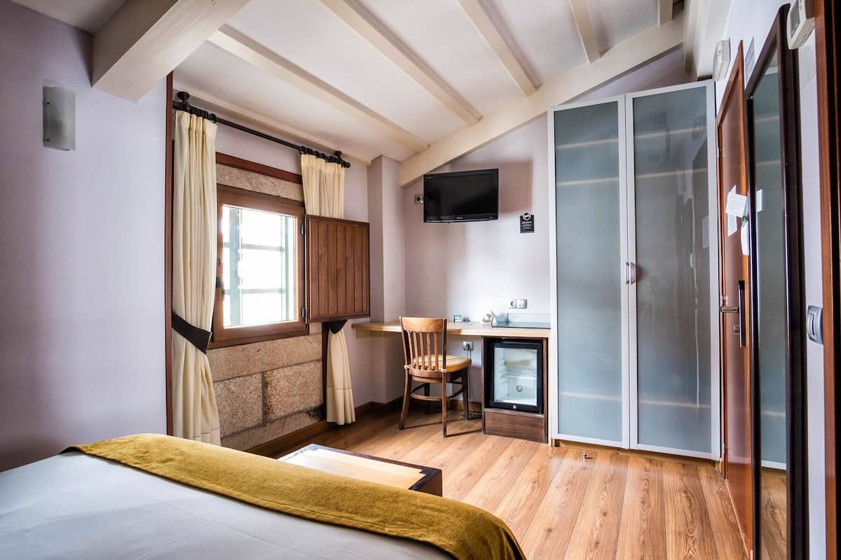 A bedroom with a bed, a desk, a chair, a TV, and a wardrobe.