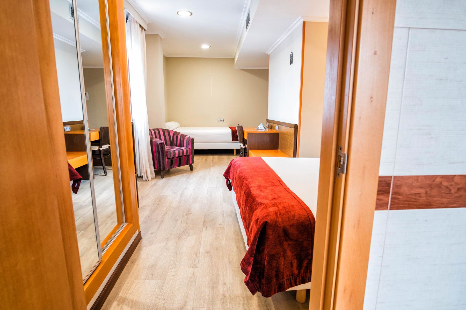 Et hotelværelse med en seng, en stol, et skrivebord og et spejl.