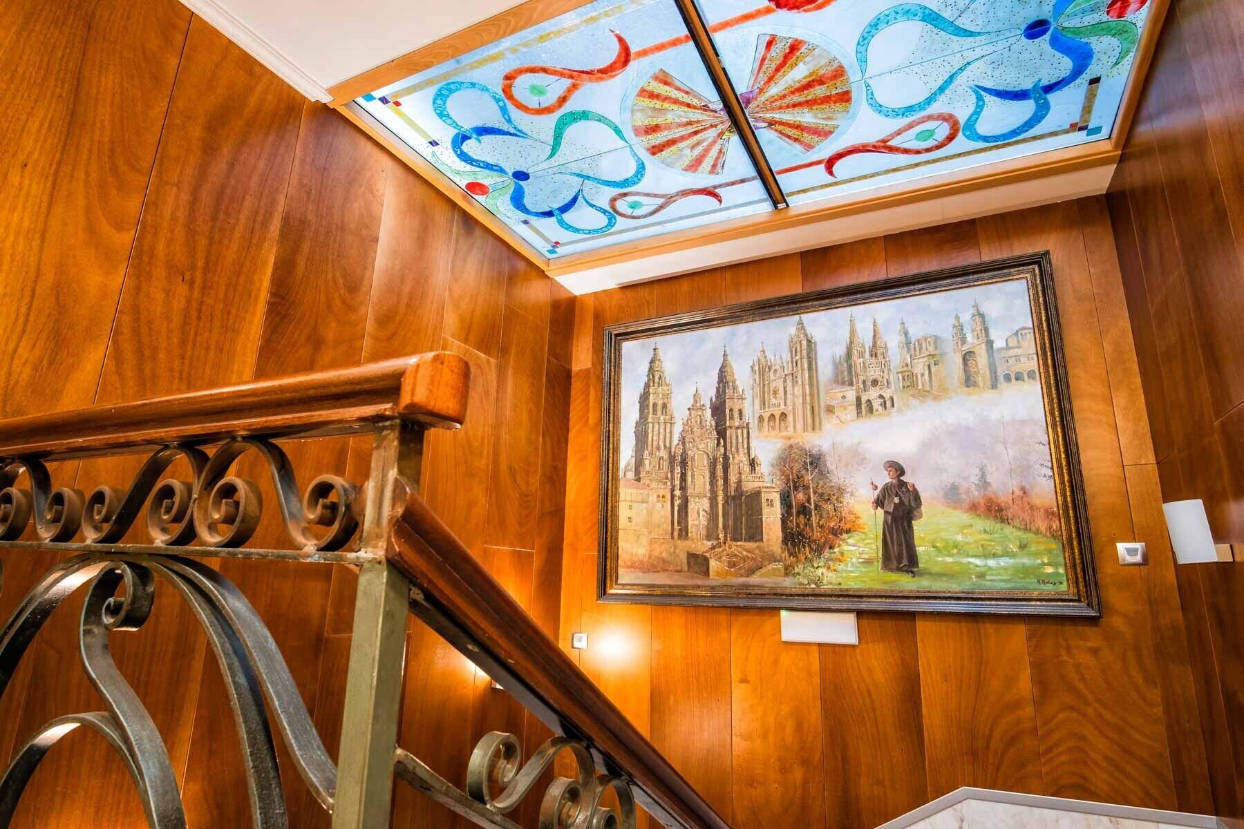 Eine holzgetäfelte Wand mit einem gerahmten Gemälde einer Kathedrale und einem Buntglasfenster über einer Treppe.