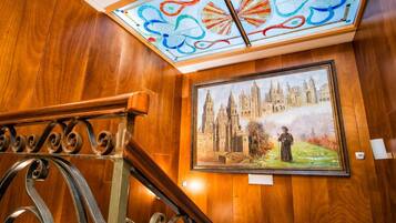 Eine holzgetäfelte Wand mit einem gerahmten Gemälde einer Kathedrale und einem Buntglasfenster über einer Treppe.