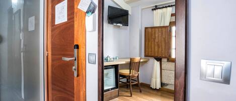 Una habitación con puerta de madera, una kitchenette pequeña con refrigerador, un televisor montado en la pared y un armario de madera.