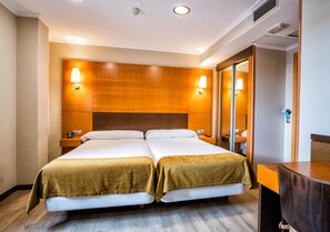 Une chambre d’hôtel avec deux lits, des têtes de lit en bois, des lampes de chevet, un grand miroir et une commode en bois.