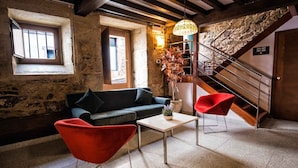 Une pièce chaleureuse avec un mur en pierre, un escalier en bois, un canapé, un fauteuil rouge et une table sur laquelle est posé un vase de fleurs.
