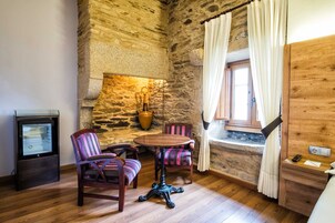Una habitación rústica con paredes de piedra, una mesa de madera, dos sillas a rayas, una radio antigua y una ventana con cortinas.