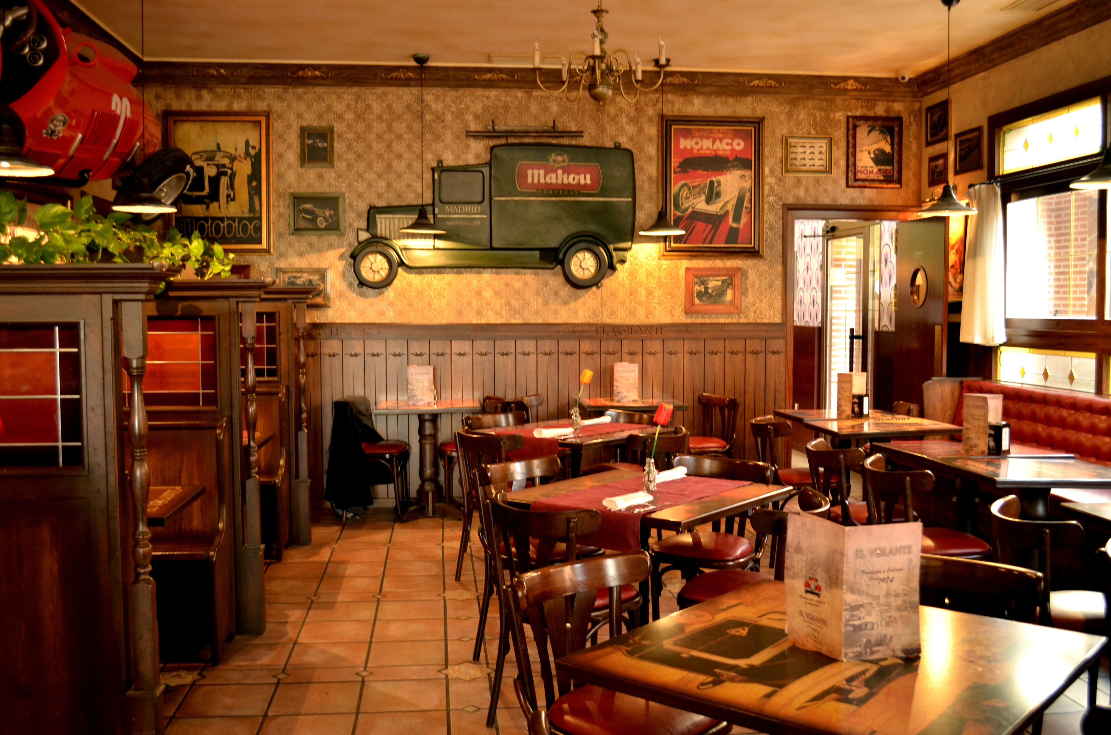 A restaurant interior with wooden tables and chairs, a vintage truck decoration, and a red booth seating area.