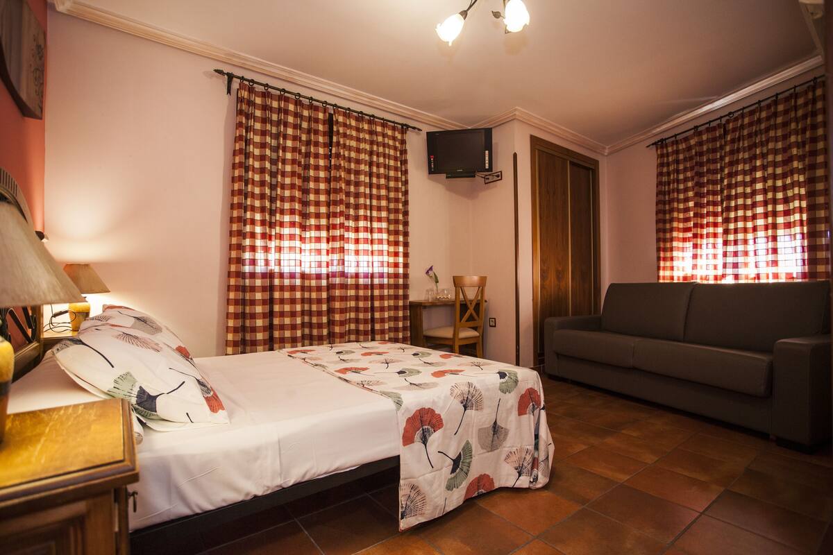 Quarto com cama, sofá, televisão e cortinas.