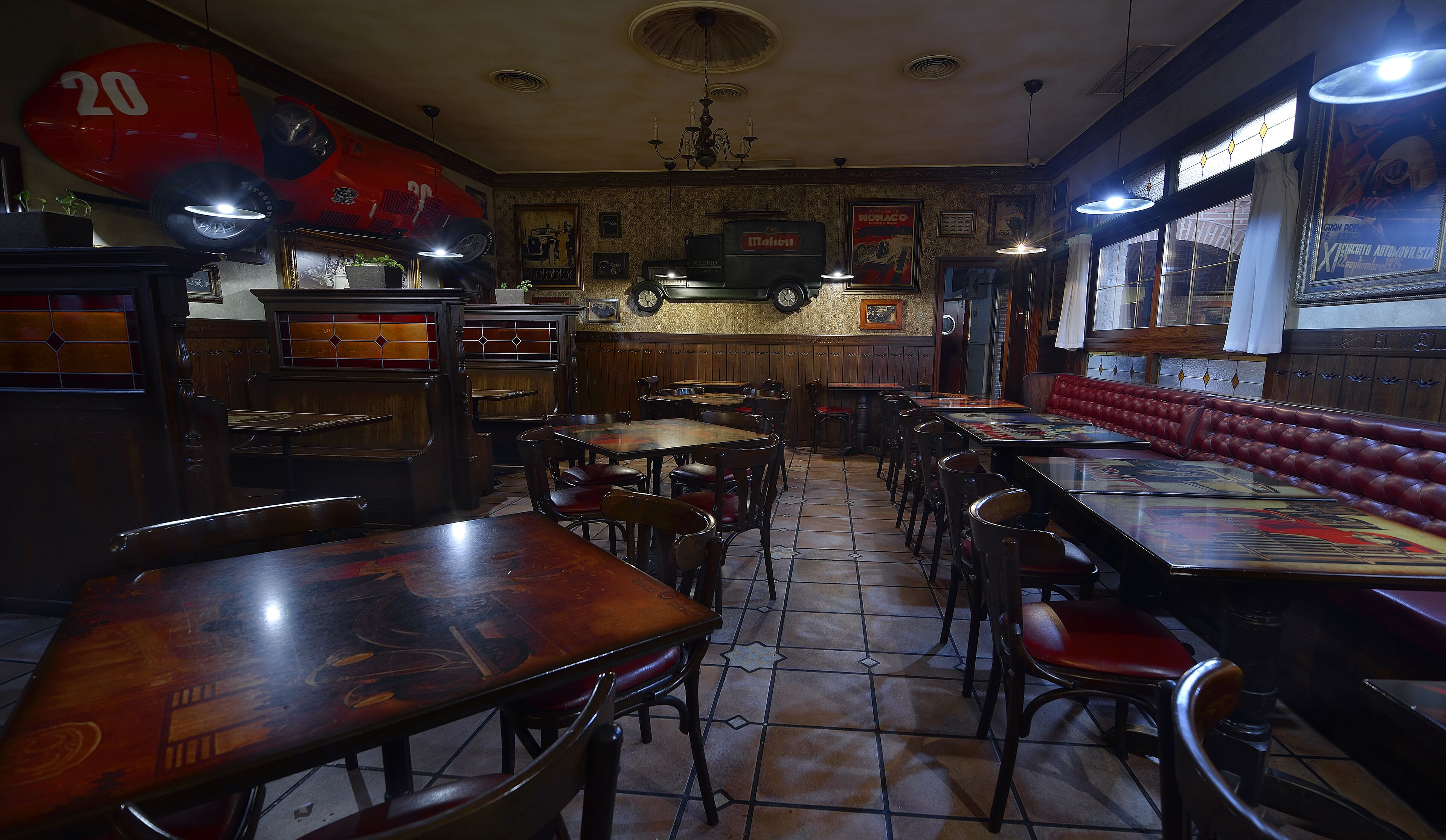 Een restaurantinterieur met houten zitbanken, hoge tafels en een decoratie van een oldtimer op de muur.