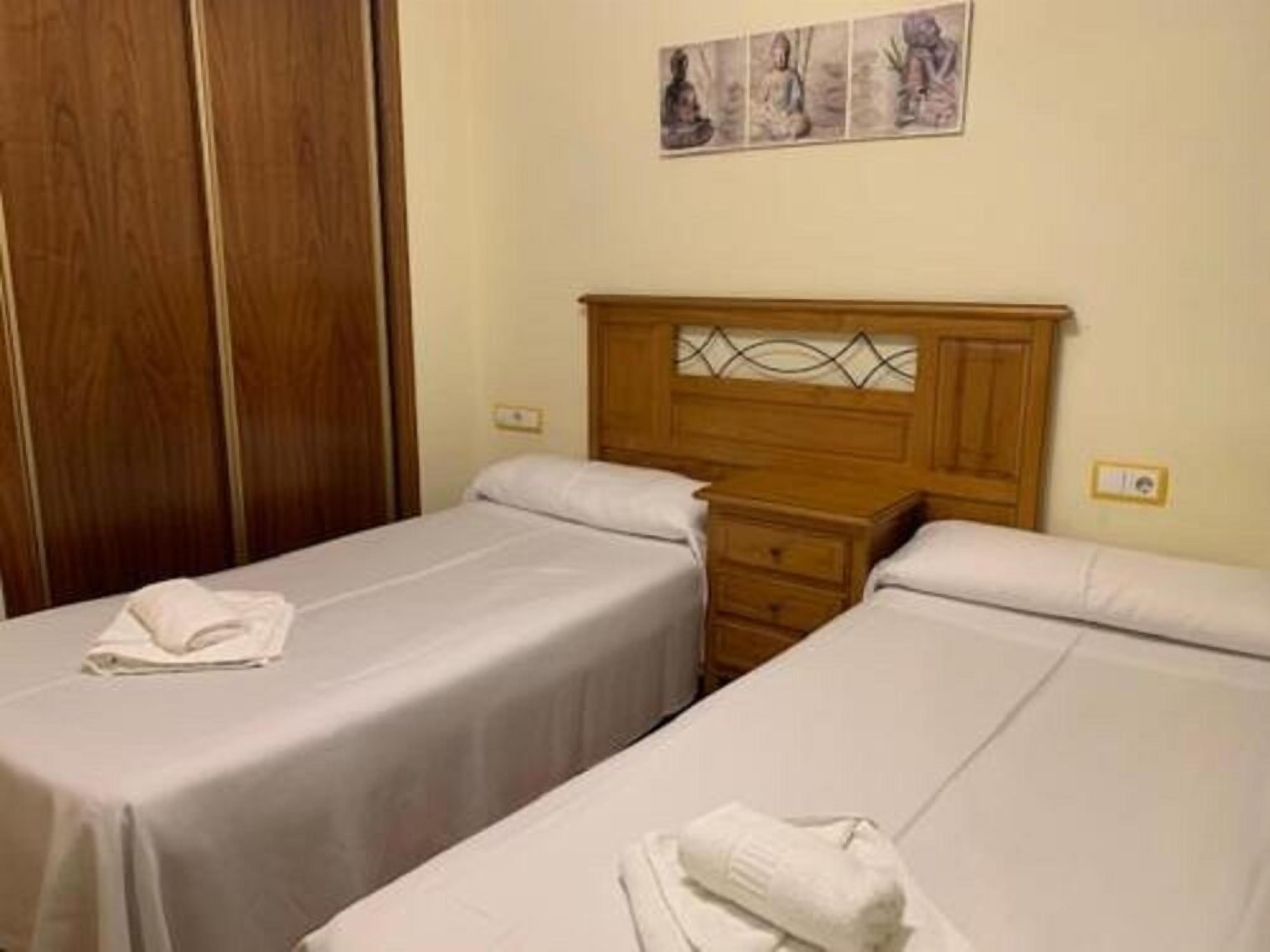 A room with two single beds, wooden headboards, and a nightstand between them.
