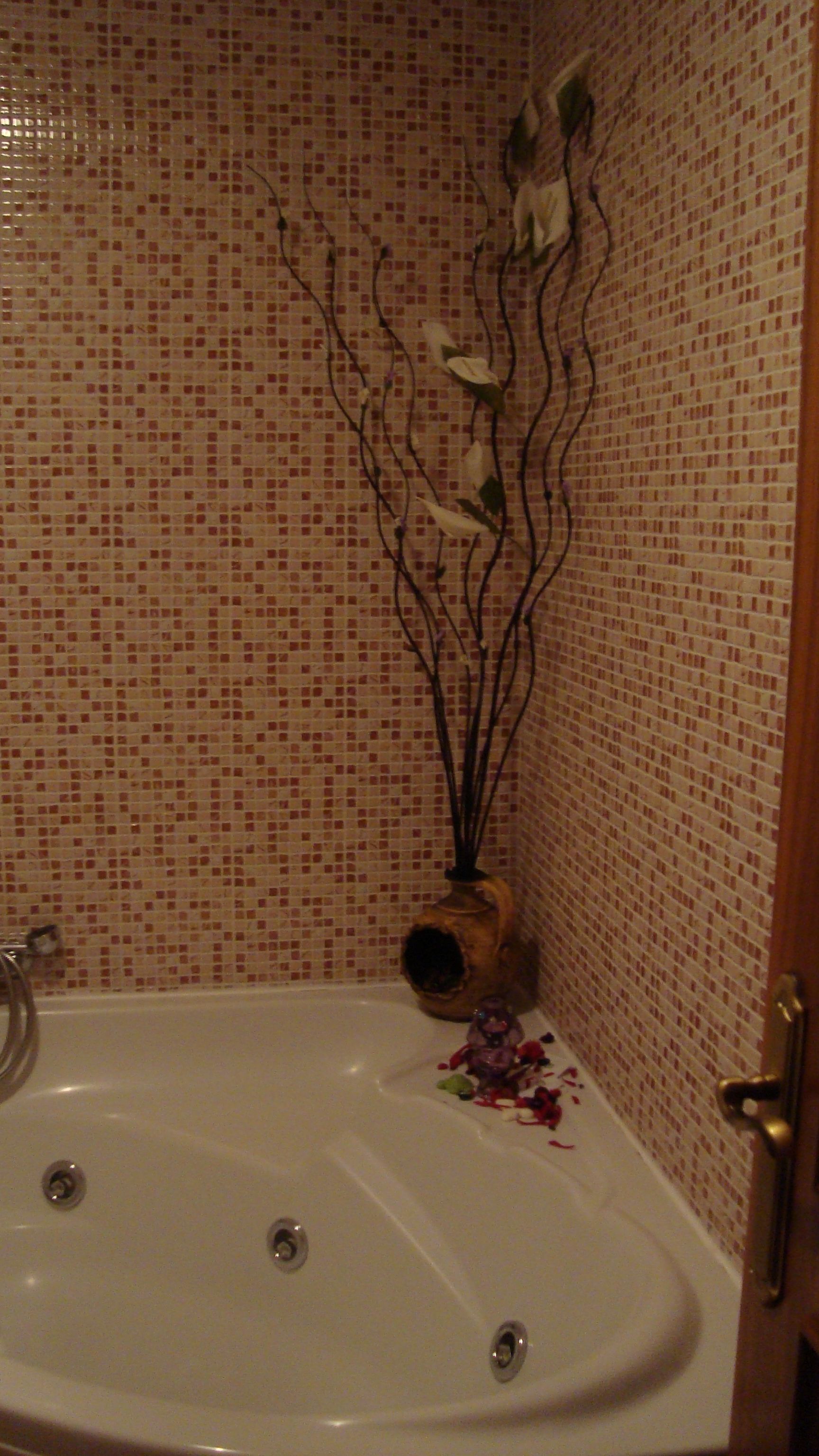 Ein Badezimmer mit einer weißen Badewanne, einer gefliesten Wand und einer dekorativen Vase mit Zweigen.