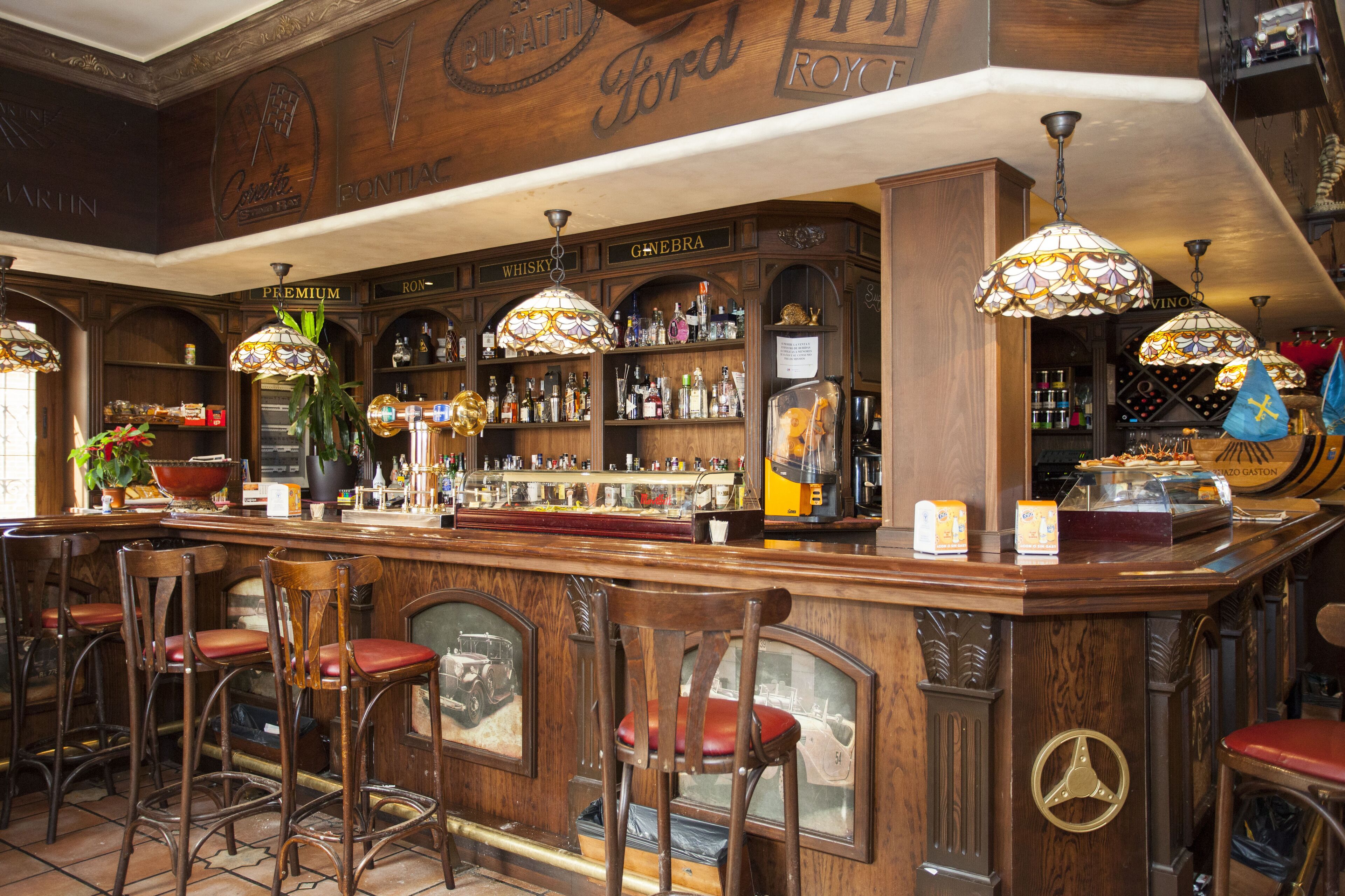 A bar area with wooden bar counter, multiple stools, and hanging lamps.