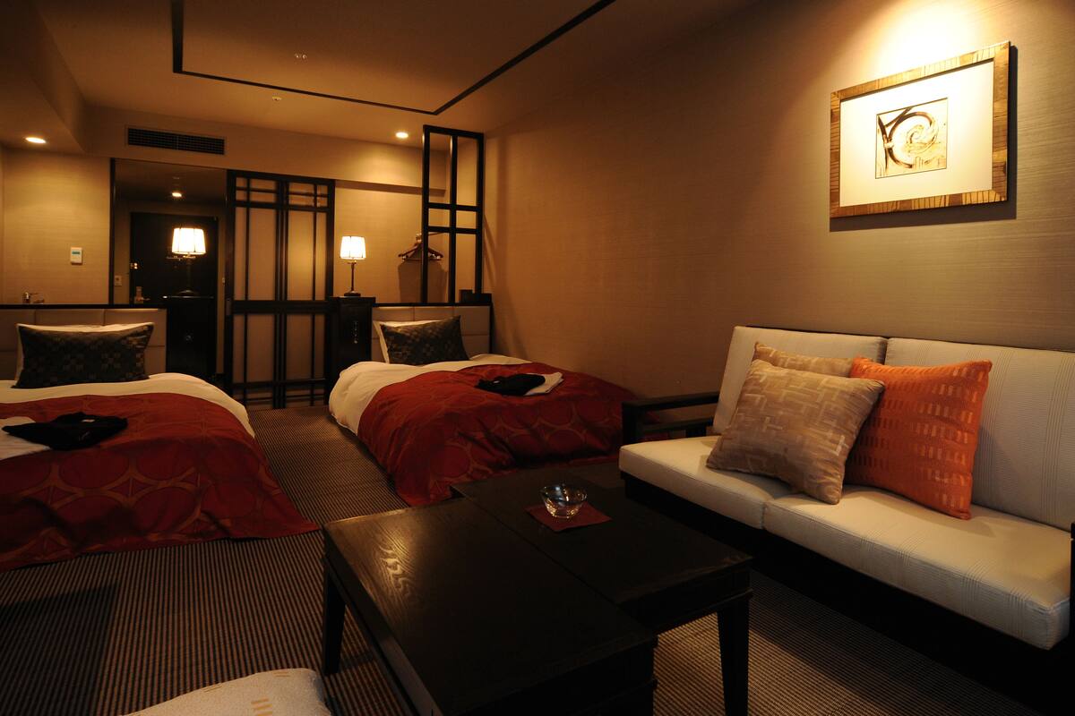 Habitación de hotel con dos camas, un sofá, una mesa de centro y una obra de arte colgada en la pared.