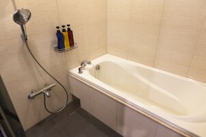 Un baño con bañera, ducha y estante con artículos de aseo.