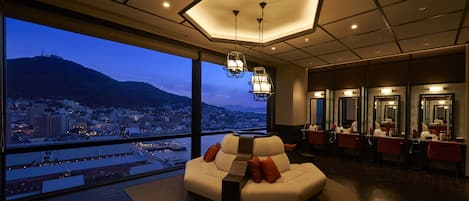 A modern hotel room with a large window offering a city view, a comfortable seating area, and a well-lit reception desk.