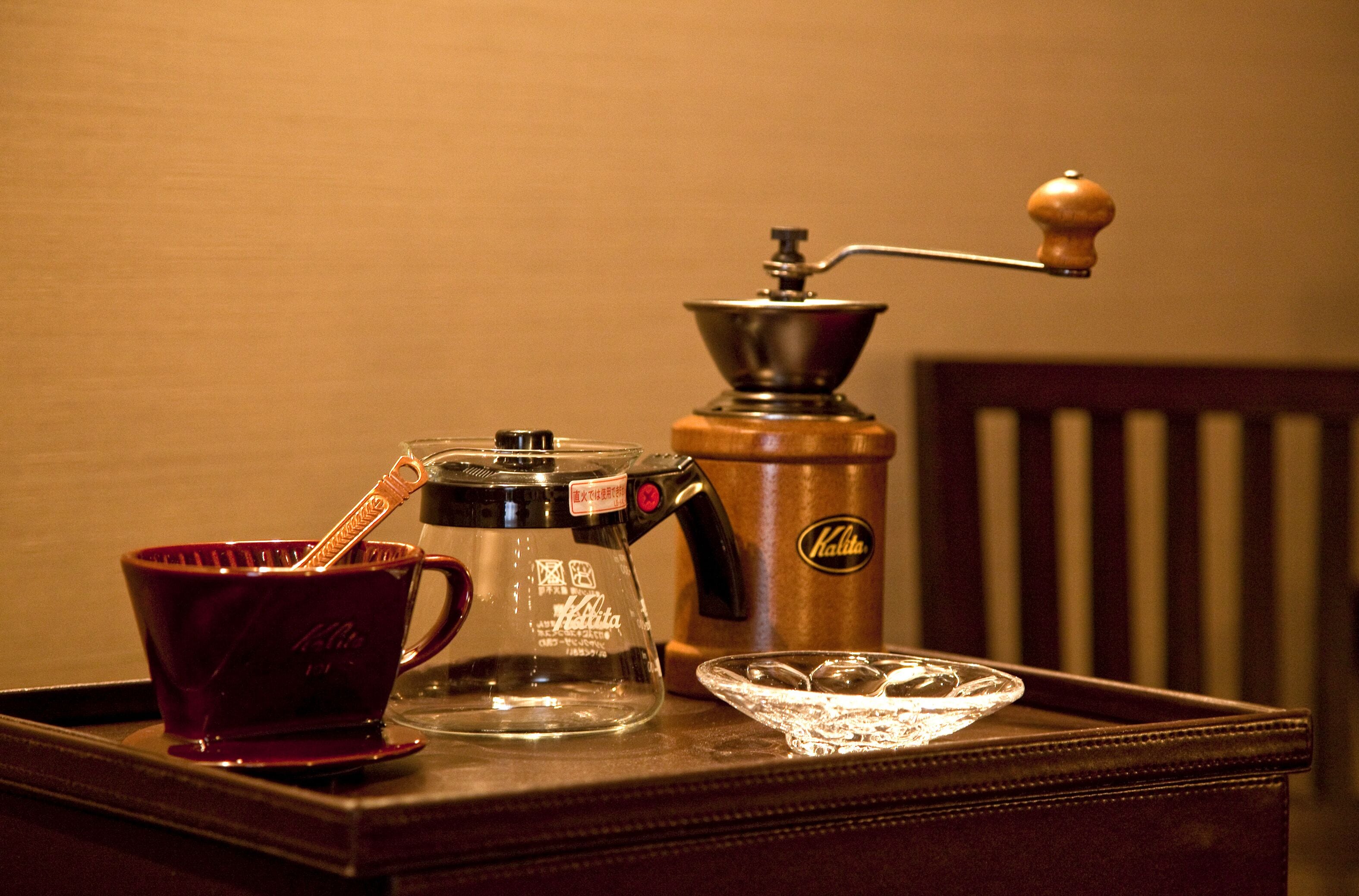 A coffee maker, a glass cup, and a tray with a glass bowl on a wooden table.