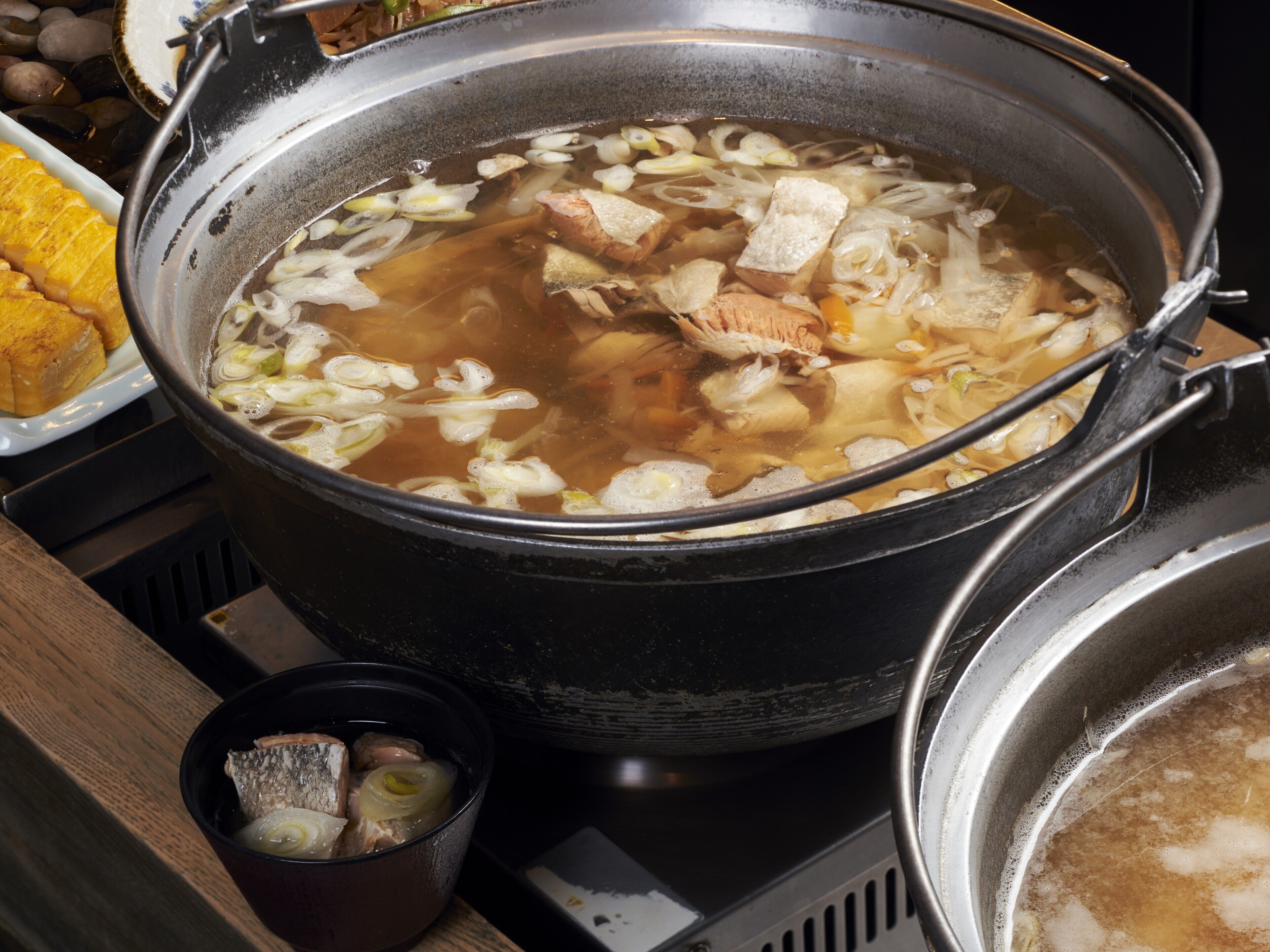 Une grande marmite de soupe contenant divers ingrédients, un bol plus petit avec un couvercle et une assiette avec différents plats.