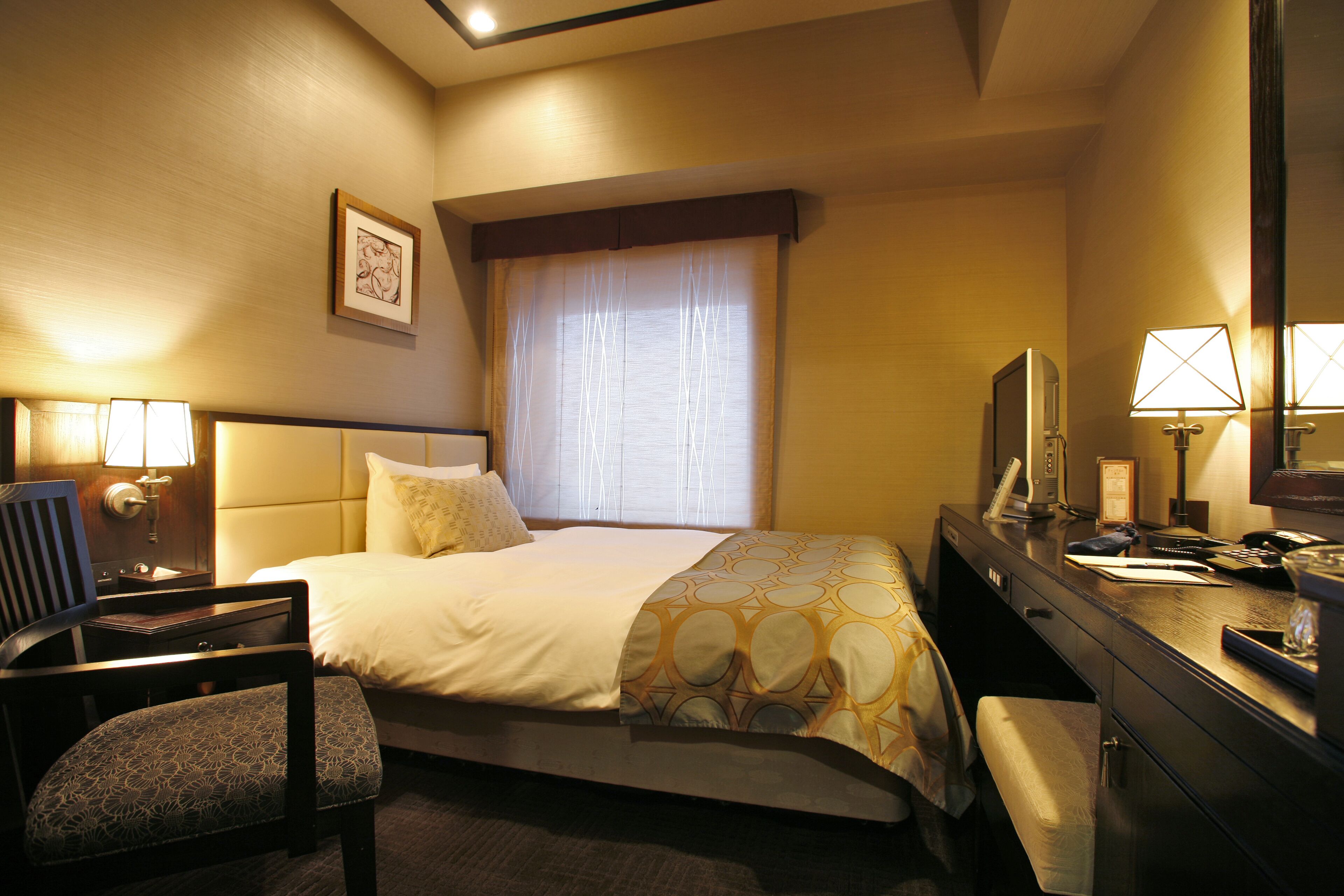 A hotel room with a bed, a desk, a chair, a television, and a window with curtains.