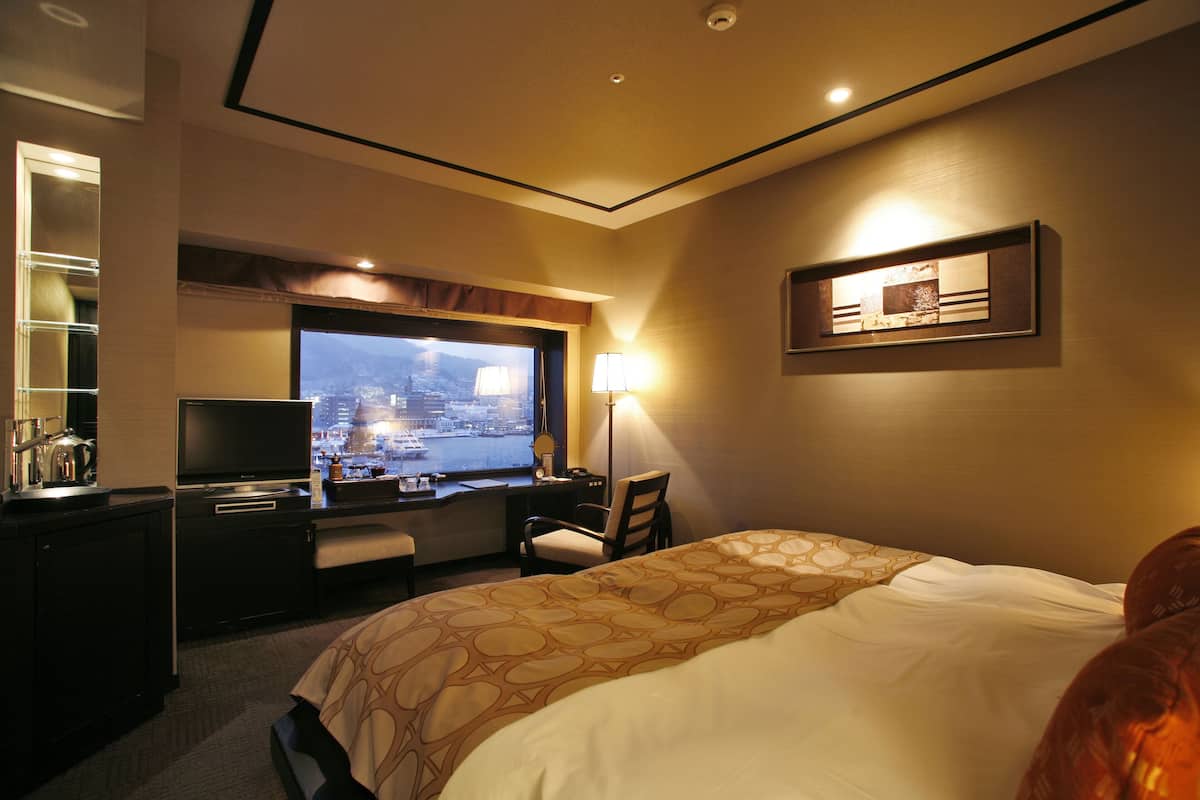 Habitación de hotel con cama, escritorio, televisión y ventana con vistas a la ciudad.