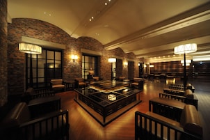 A spacious lobby with a central glass-top table surrounded by seating, brick walls, and wall-mounted lamps.