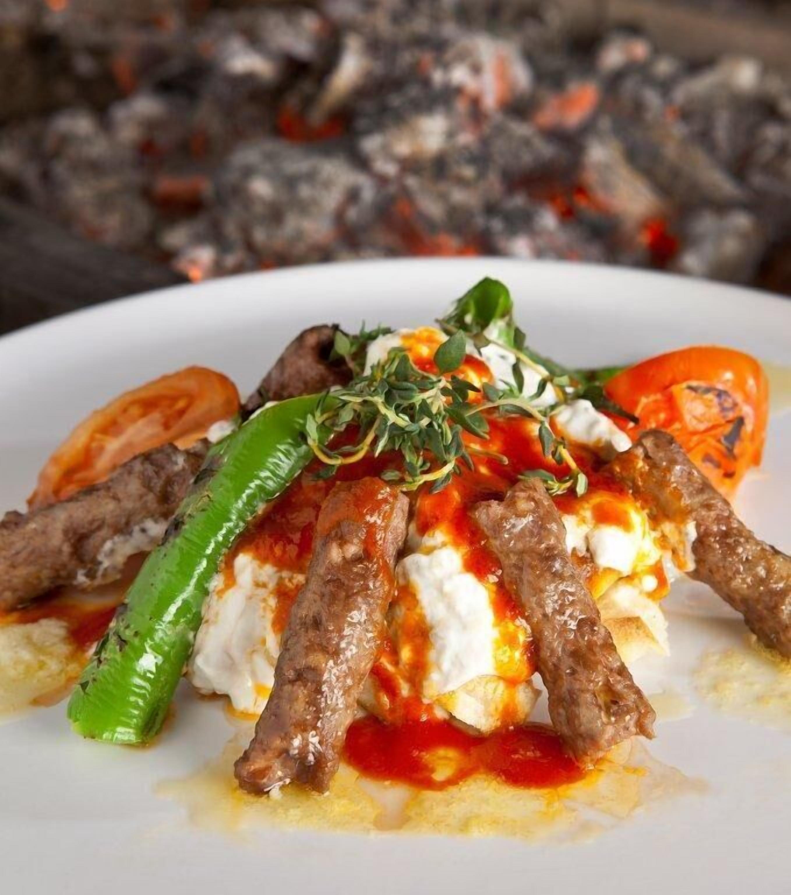 A plate of food with meat skewers, tomatoes, and a dollop of sauce.