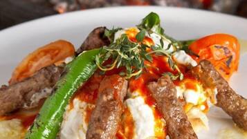 A plate of food with meat skewers, tomatoes, and a dollop of sauce.