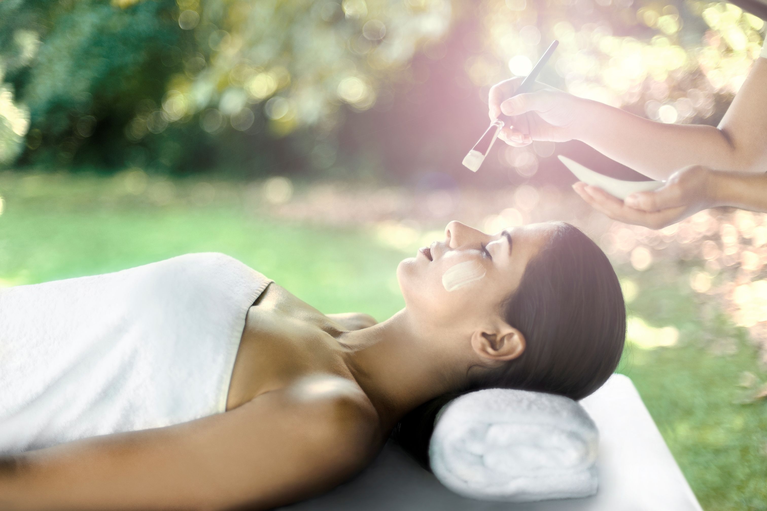 A person lying on a massage table outdoors with a towel on their head, receiving a treatment.