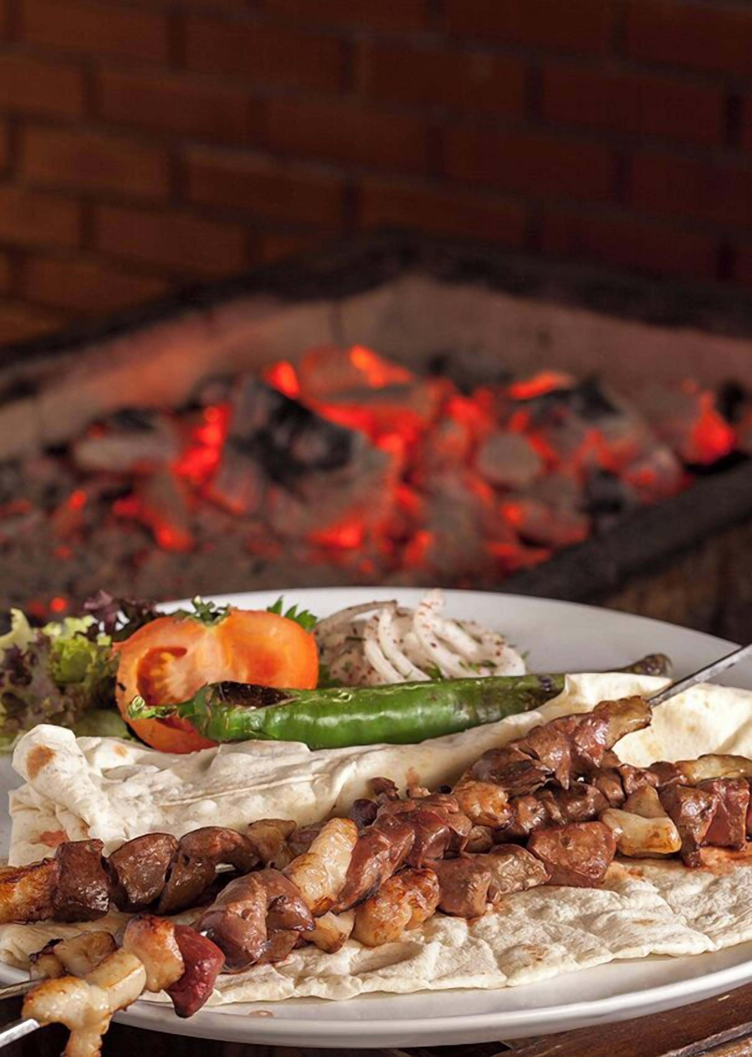 A plate of grilled meats and vegetables, with a brick oven in the background.