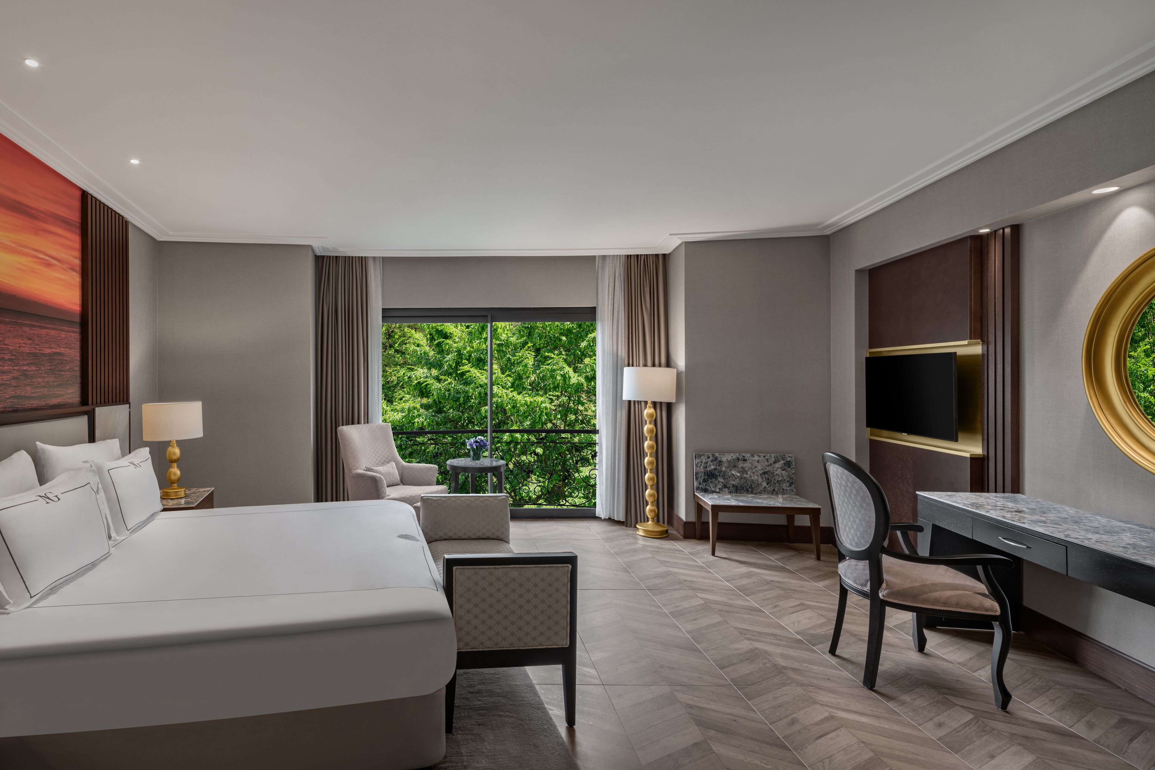 Habitación de hotel con una cama grande, un escritorio, una silla y un televisor. Tiene un balcón con vistas a zonas verdes.