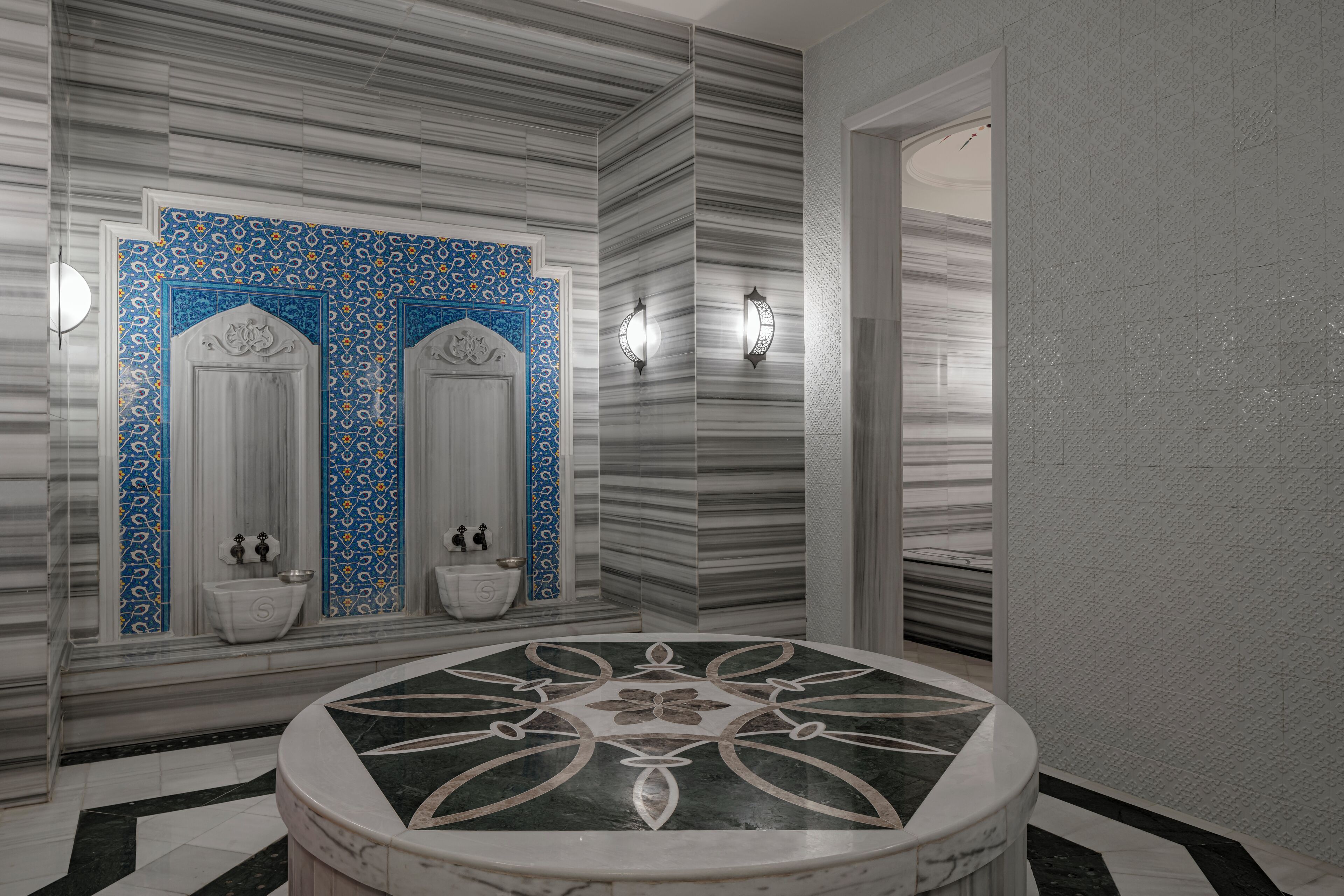 A bathroom with two sinks, a round marble bathtub, and patterned walls.