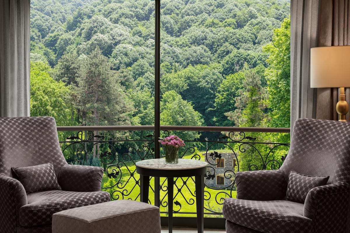 Ein Balkon mit zwei Sesseln, einem kleinen Tisch mit Blumenvase und Blick auf einen dichten Wald.