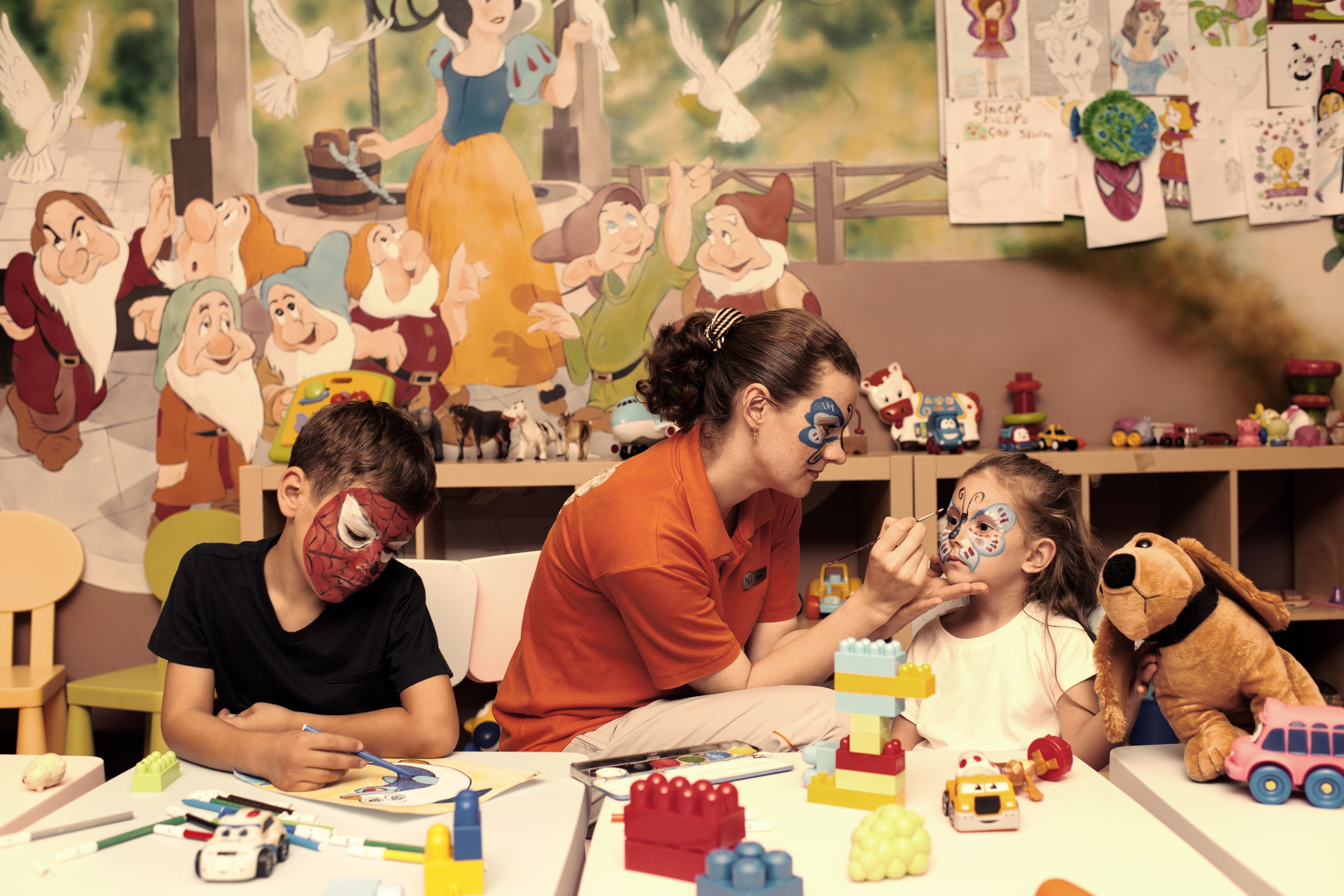 A room with a large window, a white table, and various children's toys and art supplies.
