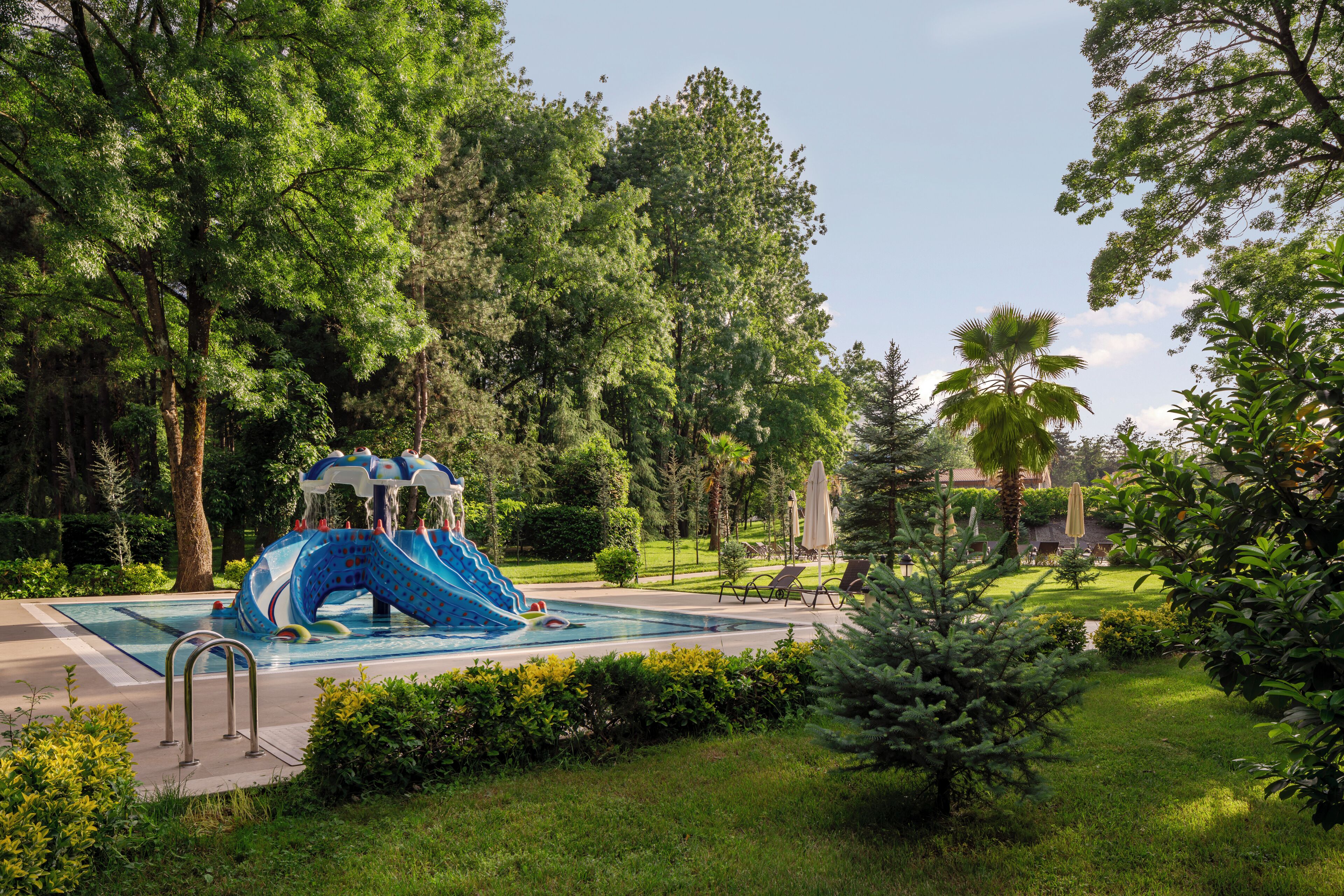A pool area with a blue water slide, surrounded by lush greenery and trees.