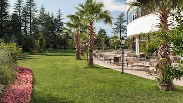 Un espace extérieur aménagé avec une terrasse bien entretenue, dotée de coins salon, et entouré d’une végétation luxuriante et d’arbres.