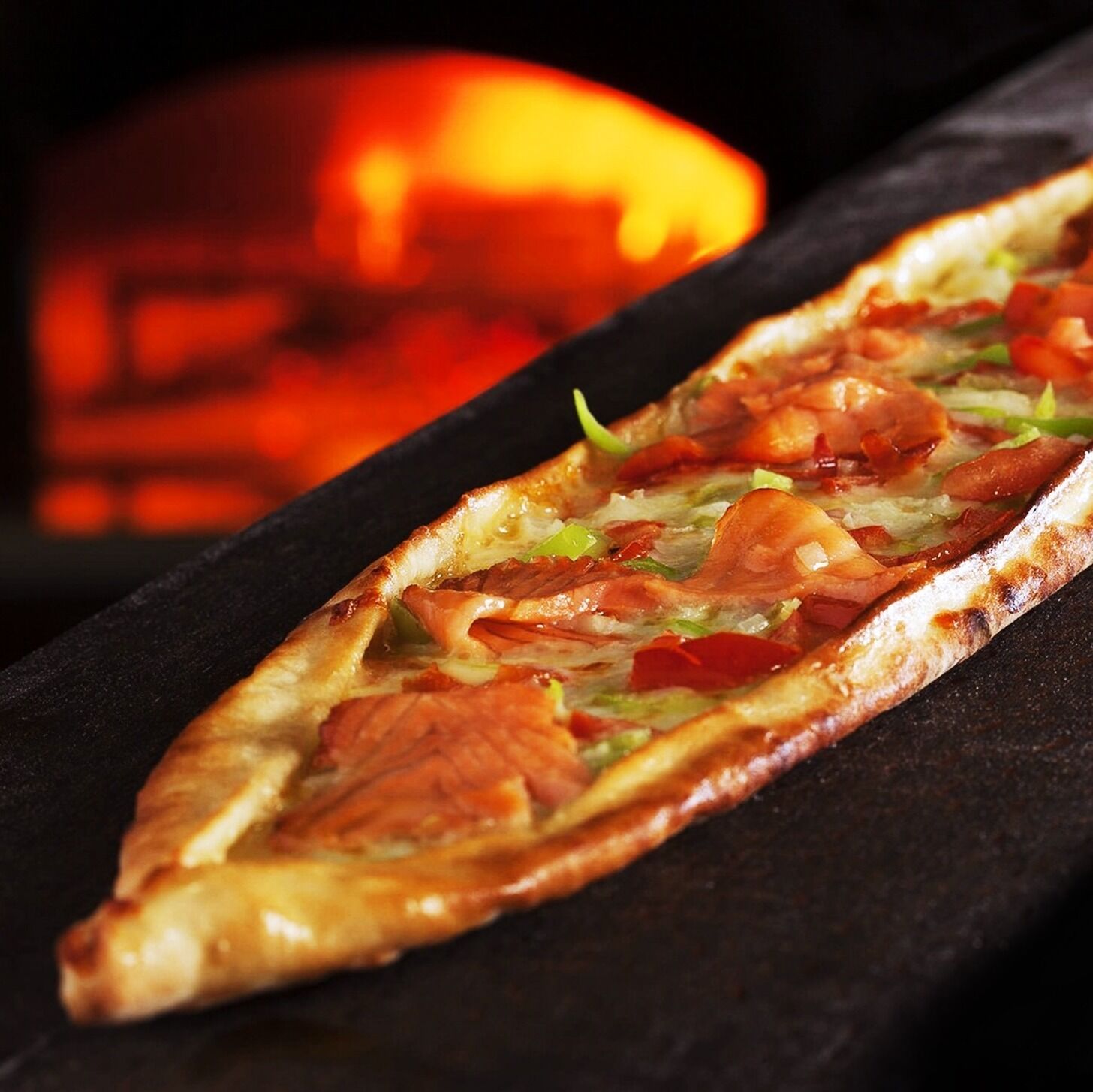 A pizza with various toppings on a black slate.