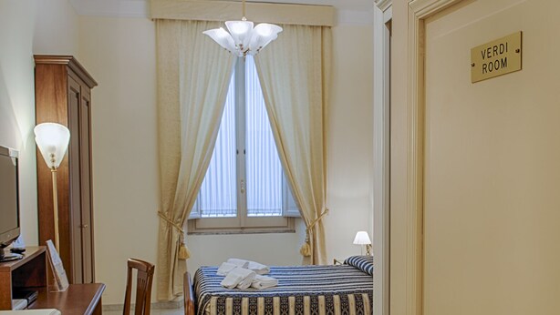 Une chambre d’hôtel équipée d’un lit, d’un bureau, d’une chaise, d’une télévision et d’une fenêtre avec des rideaux.
