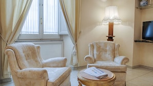 Een kamer met twee fauteuils, een tafel met een lamp en een televisie aan de muur.