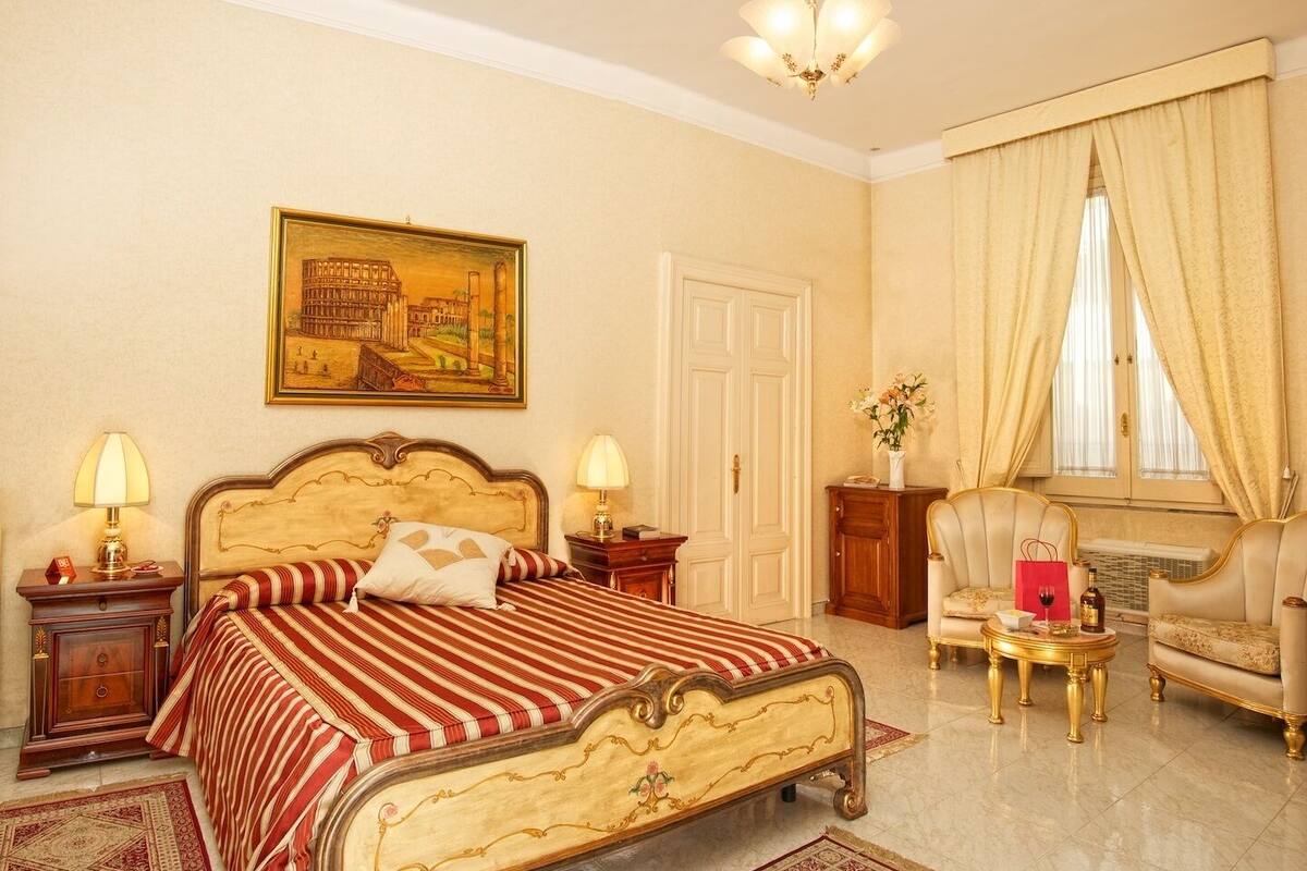 A spacious bedroom with a large bed, two bedside tables, a nightstand, a chair, a desk, and a window with curtains.