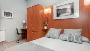 Une chambre d’hôtel moderne avec un lit, un bureau et une chaise. Il y a deux oreillers sur le lit et une plante en pot sur le bureau.