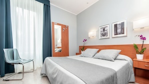 Une chambre d’hôtel comprenant un lit, une chaise, une table de chevet, un miroir et deux lampes fixées au mur.